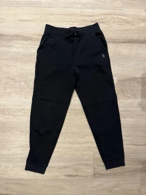 Svarta mjukisbyxor från Polo Ralph Lauren - Säljer ett par svarta mjukisbyxor från Polo Ralph Lauren med dragsko i midjan och fickor på sidorna. Byxorna har en avslappnad passform och den klassiska loggan broderad på vänster sida. Perfekta för chill dagar eller när du vill vara bekväm.