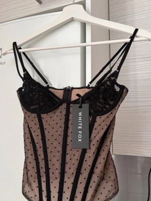Svart mesh korsett topp - Trendig svart korsett från White Fox i mesh med prickigt mönster och dekorativa spetsdetaljer vid bysten. Justerbara axelband och markerade sömmar ger en snygg siluett. Den är helt oanvänd, säljer därför det tyvärr passar inte mig😩🙏🏼