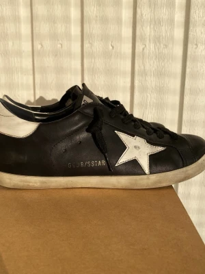 Svarta Golden Goose sneakers med stjärna - Säljer nu min riktigt feta golden goose skor med en liten defekt i sulan samt lite ut suddad text där bak annat lite smutsiga ba 8/10 skick. Skriv vid minsta fråga 😇