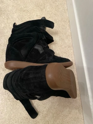 Svarta höga sneakers med kardborre - Snygga svarta sneakers med högt skaft och kardborreband. Skorna har en cool design i mocka och detaljer i läder, samt en brun gummisula som ger kontrast. Perfekta för dig som gillar streetstyle och vill sticka ut lite extra.