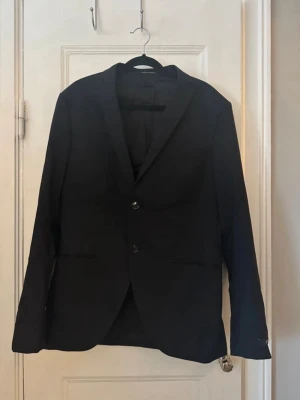 Svart kavaj - Tiger of Sweden - Storlek 48 - Herr - Stilren svart kavaj med två knappar framtill och klassisk krage. Kavajen har två fickor och är helfodrad. Passar perfekt till skjorta eller t-shirt för en clean look. 