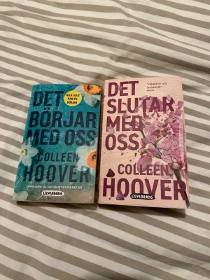 Det börjar med oss & Det slutar med oss - Två populära romaner av Colleen Hoover: 'Det börjar med oss' med blått och orange blommigt omslag och 'Det slutar med oss' med rosa och lila blommigt omslag. Båda är pocketböcker på svenska och utgivna av Lovereads.