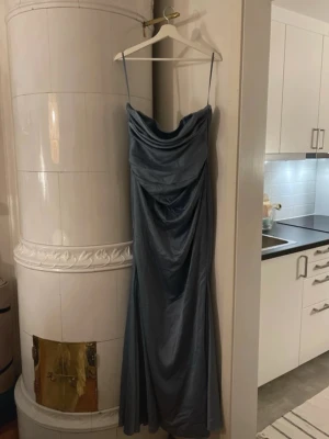 Balklänning - Elegant axelbandslös långklänning i blå satin med draperade detaljer framtill och smickrande passform. Klänningen har en figurnära siluett och vacker rynkning vid midjan och ryggen. Perfekt för fest eller bal. Helt oanvänd och fortfarande i original förpackning 🌟köpt för 1600kr men säljer för 750kr!!