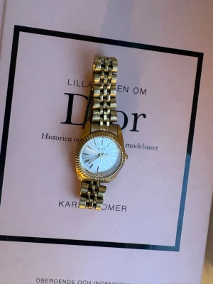 Guldfärgad klocka från Regal - Stilren guldfärgad klocka från Regal med klassisk länkarmband och rund vit urtavla. Klockan har tydliga markeringar och en elegant design som passar till många olika stilar.