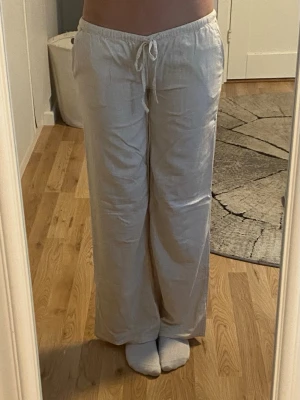 Beiga linnebyxor med dragsko - Säljer ett par beiga linnebyxor från H&M med avslappnad passform och dragsko i midjan. Byxorna har raka ben och resår i midjan för extra komfort. Perfekta för en chill och stilren look. De är nedsydda ca 4cm så de sitter lowwaisted ( se bild) 