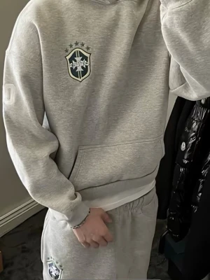 Gråa mjukisbyxor med emblem Brazilian style  - Säljer ett par gråa mjukisbyxor med elastisk midja och ett snyggt emblem på vänstra benet. Byxorna har avslappnad passform och är gjorda i mjuk bomullsblandning som känns skön mot huden. Perfekta för chill dagar eller när du vill ha en casual look.