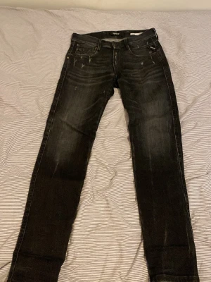 Svarta Replay slim fit jeans - Säljer ett par svarta slim fit jeans från Replay med diskreta slitningar och snygg tvätt. Jeansen har klassisk femficksmodell, normal midja och smala ben. Materialet är mjukt och stretchigt för extra komfort. Perfekta för dig som gillar en modern och stilren look.