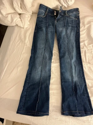 Mörkblå bootcut jeans med pressveck - Snygga mörkblå bootcut jeans med markerade pressveck framtill. Jeansen har klassisk femficksdesign, dubbla knappar i midjan och kontrastsömmar. Tillverkade i denim med lätt stretch för skön passform. Jag har sytt dit två hakar men går säkert att ta bort 