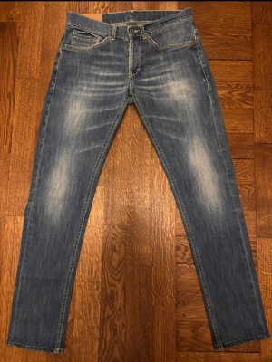 Blå dondup George jeans - Snygga blå slim fit jeans med slitna detaljer och ljusa tvättade partier på låren och knäna. Modellen heter George. Klassisk femficksmodell med dragkedja och knapp i midjan. Jeansen har en modern passform och är perfekta för en avslappnad stil. Väldigt fint skick me skön passform, kolla in min profil för fler liknande par!