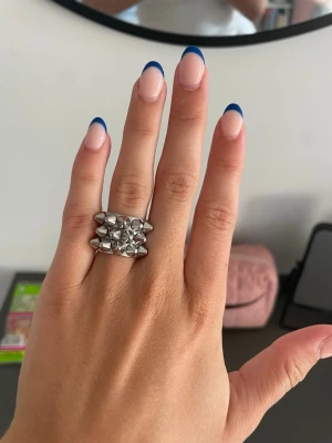 Silvrig ring med nitar Edblad 16.00 - Cool och chunky ring i silverfärgad metall med flera spetsiga nitar runt hela ringen. Ringen har en bred design och ger en edgy känsla till din stil. Perfekt för dig som gillar statement-smycken och vill sticka ut.