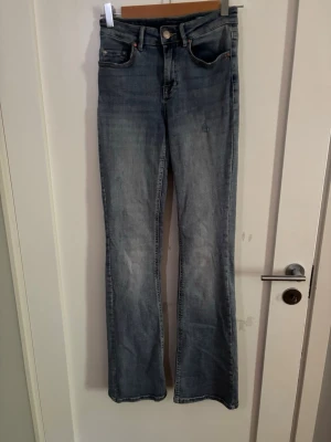 Ljusblå bootcut jeans - Säljer ett par ljusblå bootcut jeans med klassisk femficksdesign och normal midja. Jeansen har en lätt tvättad look och är tillverkade i denim med lite stretch för skön passform. Perfekta till sneakers eller boots. Storlek 34