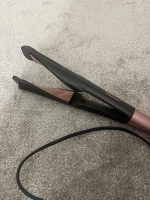 Remington plattång svart/roséguld - Säljer en snygg plattång från Remington i svart och roséguld. Plattången har sladd och keramiska plattor med räfflad kant, perfekt för att styla håret. Enkel knapp för att slå på och av. Passar dig som vill fixa frisyren snabbt och smidigt.