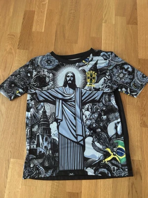 Neymar Brasil tröja - Jag säljer en svart t-shirt med Neymar Jr. och nummer 10 på ryggen. Framsidan har ett stort tryck av Kristusstatyn i Rio, brasilianska flaggan och detaljerade svartvita mönster. Korta ärmar och rund hals. 