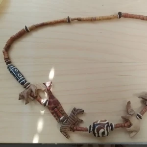 Halsband med träpärlor och djurmotiv - Unikt halsband med handgjorda träpärlor och detaljerade träfigurer av savannens djur som giraff, noshörning, zebra och elefant. Färgerna går i brunt, beige och svart med inslag av mönstrade pärlor. Perfekt för dig som gillar naturinspirerade accessoarer.