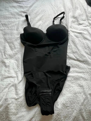 Svart body med bygel och vaddering - Snygg svart body med vadderade kupor och bygel för extra stöd. Justerbara axelband och knäppning i grenen. Tillverkad i 81% polyamid och 19% elastan för en stretchig och bekväm passform.