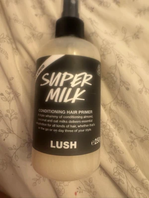 LUSH Super Milk Conditioning Hair Primer - Super Milk Conditioning Hair Primer från LUSH är en hårvårdsprodukt i sprayflaska med svart och vit etikett. Innehåller mandel-, kokos- och havremjölk för att återfukta alla hårtyper. Flaskan rymmer 250 ml och är perfekt för att ge håret extra fukt och vård. Det finns cirka 70% procent kvar i burken 