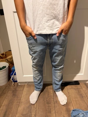 Ljusblå slim fit jeans herr nudie jeans  - Säljer ett par ljusblå slim fit jeans med klassisk femficksdesign och diskreta slitningar på framsidan. Jeansen har normal midja och raka ben, perfekta för en avslappnad och trendig look. Tillverkade i mjukt denimtyg för extra komfort.