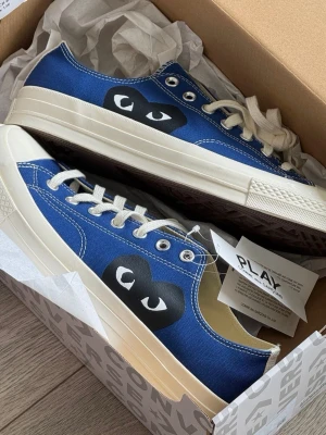 CDG Converse low blue  - Säljer ett par COMME des GARÇONS PLAY x Converse  i blå färg, storlek 44. Skorna är i mycket bra skick och har använts sparsamt. Klassisk modell med den ikoniska hjärtloggan på sidan. Perfekta till både vardag och streetwear.