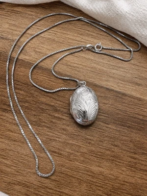  Ovalt medaljonghalsband i 925 silver - Snyggt halsband i sterling silver med en oval medaljong som har ett detaljerat, graverat blommönster på framsidan. Kedjan är tunn och boxlänkad, vilket ger ett stilrent och elegant intryck. Perfekt för dig som gillar klassiska accessoarer med en twist.