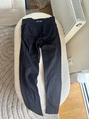 Svarta leggings från DFYNE - Snygga svarta leggings från DFYNE med hög midja och ribbad linning. De är tighta och stretchiga, perfekta för träning eller chill. Materialet känns mjukt och följsamt mot kroppen. Klassisk svart färg som passar till allt. Finns ett hål i Scrunchen som syns på bilden, syns bara i vissa övningar 