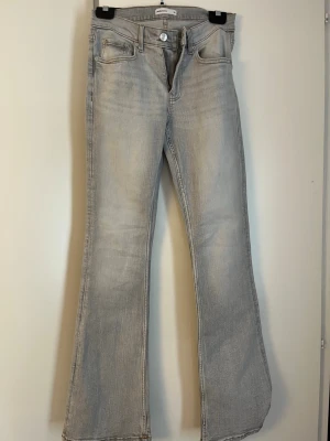 Ljusgrå bootcut jeans - Säljer ett par ljusgrå bootcut jeans med klassisk femficksmodell och utsvängda ben. Jeansen har knapp- och dragkedjestängning samt bälteshällor. Perfekta för dig som gillar en retroinspirerad look och vill ha ett par bekväma jeans i mjukt denimtyg.