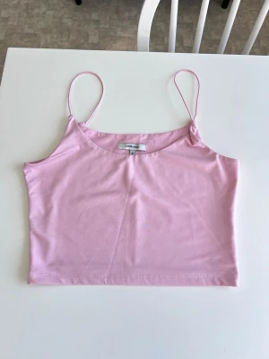 Ljusrosa crop top med smala axelband - Ett ljusrosa/babyrosa croppat linne med smala axelband, från Chiquelle. Storlek M, men mer som en S.  Säljer pga att det inte komme till användning. Höger axelband sitter på med några enstaka trådar men går att sy fast bättre, se bilder.