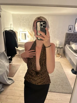 Leopardmönstrad halterneck topp - Säljer en leopardmönstrad halterneck topp med djup urringning och öppen rygg. Toppen har en loose passform och är perfekt för dig som vill sticka ut. Tyget känns mjukt och följsamt, troligen i polyester eller syntetmaterial.