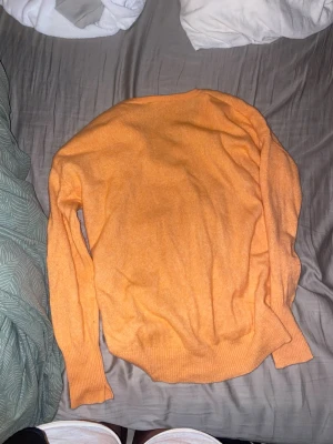 Orange stickad tröja med V-ringning - En mjuk och skön orange stickad tröja med V-ringad hals och långa ärmar. Tröjan har ribbstickade muddar vid ärmslut och nederkant. Perfekt för att addera färg till din outfit.