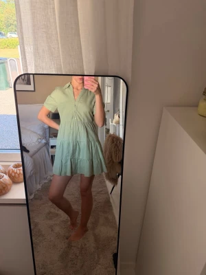 Ljusgrön kort klänning med knappar - Söt ljusgrön kortklänning med krage och knappar framtill. Klänningen har korta ärmar och volangdetaljer i kjolen för en avslappnad look. Tillverkad i ett mjukt material som känns skönt mot huden. Perfekt för varma dagar. Aldrig använt men lappen har gått av( se sista bild)🤍