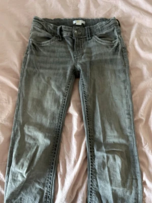Grå jeans med kontrastsömmar - Säljer ett par grå jeans med raka ben och snygga kontrastsömmar på bakfickorna. Jeansen har klassisk femficksmodell och knappgylf. Materialet är denim i bomull. Perfekta för en avslappnad och trendig look.