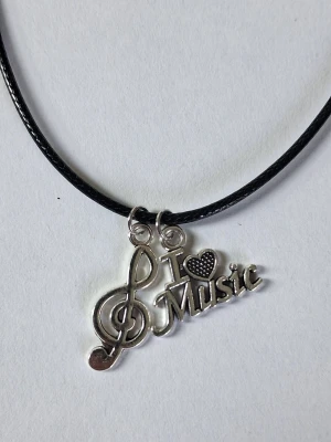 Halsband med I Love Music-hänge - Vaxat läderhalsband och två silverfärgade hängen i form av en G-klav och texten 'I ♥ Music'. Perfekt för dig som älskar musik och vill visa det med stil. Hängena är detaljerade och ger en cool touch till din outfit.