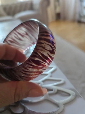 Bredt armband med zebramönster - Säljer ett coolt, brett armband i plast med glittrigt zebramönster i rött och guld. Armbandet har en rund form och en blank finish som fångar ljuset snyggt. Perfekt för dig som vill sticka ut med accessoarerna!