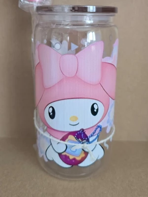 Glasburk med My Melody-motiv - Söt glasmugg med tryck av My Melody i rosa och vitt. Burken har ett lock och ett snöre runt om. Perfekt för förvaring av småsaker eller som dekoration. Motivet visar My Melody med stor rosa rosett och ett hjärta.