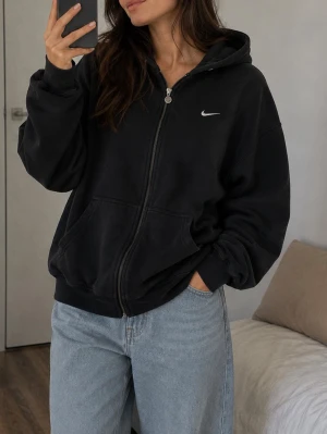 Svart Nike zip hoodie med huva - Säljer en svart zip hoodie från Nike med klassisk vit logga på bröstet. Hoodien har dragkedja framtill, kängurufickor och en skön huva. Perfekt oversized passform och mjukt material som känns riktigt bekvämt. Passar till jeans eller joggers för en chill look.Hoddie ser ut som en använd hoddie , de darför säljer den så låg. Den kan ha vissa såna små kullor på oså.Men de darför säljer så låg