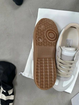  sneakers beige/vit -  sneakers i beige och vitt med klassisk gummisula. Ovandel i en mix av mocka och läder, neutrala färger och diskret design. Ikonisk sula med präglad logga och numrering. Perfekta för en clean och stilren look.