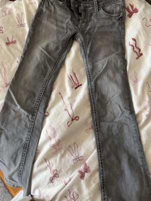Grå jeans med vita sömmar - Snygga grå jeans med raka ben och vita kontrastsömmar på bakfickorna. Klassisk femficksmodell med låg midja och dragkedja. Perfekta till en avslappnad streetstil.