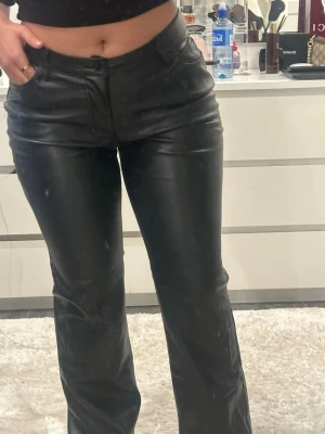 Svarta skinnbyxor med bootcut - Snygga svarta byxor i skinnimitation med bootcut-modell och klassisk femficksdesign. Byxorna har normal passform och stängs med knapp och dragkedja. Perfekta för dig som vill ha en edgy och trendig look.