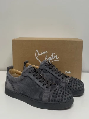 Louis Junior Spikes - Mörkgråa sneakers från Christian Louboutin med nitar. Otroligt bra skick, inga större tecken på användning. Säljes med orginallåda, dustbags, extra snören och kvitto från mytheresa.