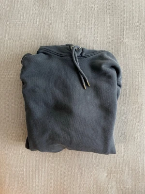 Mörkgrå hoodie med snören - En stilren mörkgrå hoodie i storlek L med luva och snören. Hoodien har en klassisk passform med fickor på sidorna.
