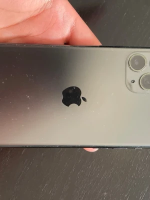 Svart iPhone med dubbla kameror - Säljer en svart iPhone med stilren design och dubbla kameror på baksidan. Mobilen har en glansig baksida i glas och den klassiska Apple-loggan i mitten. Perfekt för dig som gillar snygg och modern teknik.