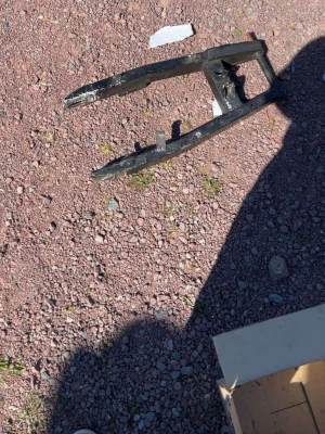 Svart metallram till fordon - En svart metallram, troligen en del till ett fordon som en moppe eller cykel. Ramen har en rektangulär form med två parallella armar och några fästen. Perfekt för dig som gillar att meka eller behöver reservdelar.