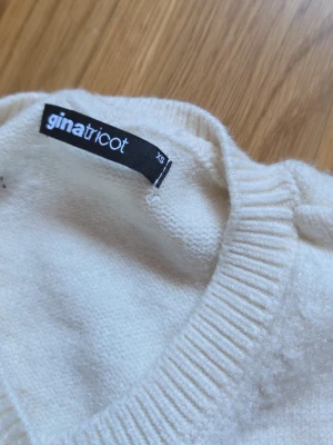 Vit kofta från Gina Tricot XS - Snygg vit kofta från Gina Tricot i storlek XS. Koftan har rund halsringning, ribbade muddar och en enkel, klassisk design. Perfekt att slänga över en topp eller klänning för en stilren look. Den är lite nopprig på ryggen