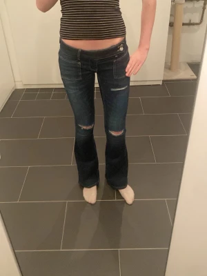 Mörkblå bootcut jeans med slitningar - Säljer ett par mörkblå bootcut jeans med slitna detaljer över knäna. Jeansen är från Gina tricot och tillverkade i stretchigt denimtyg för skön passform. Perfekta för dig som gillar en avslappnad men trendig look. Anledning till att jag säljer är att de är förkorta. Använda 3 gånger.
