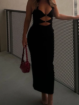 Svart långklänning med cut-outs - Trendig svart långklänning med djup urringning och snygga cut-outs framtill. Klänningen är ärmlös och har en figurnära passform som framhäver siluetten. Perfekt för dig som vill sticka ut med en stilren och modern look.