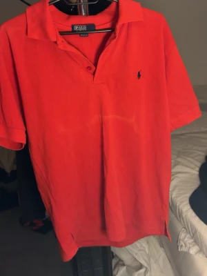 Röd pikétröja från Polo Ralph Lauren - Snygg röd pikétröja från Polo Ralph Lauren med klassisk krage och korta ärmar. Tröjan har den ikoniska broderade loggan i mörkblått på bröstet och är tillverkad i mjuk bomull. Perfekt för en avslappnad och stilren look. billigare pris för ett vitt sträck vid magen 1,5 ny