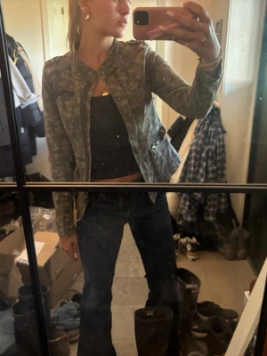 Grön camouflage jeansjacka - Snygg grön jeansjacka med camouflage-mönster och dragkedja framtill. Jackan har en figurnära passform och coola detaljer på axlarna. Perfekt för dig som vill ha en trendig och streetinspirerad look.