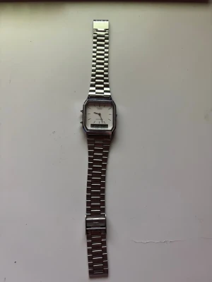 Casio silverfärgad armbandsklocka - Stilren armbandsklocka från Casio med fyrkantig urtavla och digital display. Klockan har en klassisk länk i silverfärgat metall och vit urtavla med minimalistiska markeringar. Perfekt accessoar för en clean och tidlös look.