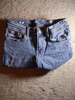 Blå jeans från Jack & Jones - Säljer ett par klassiska blå jeans från Jack & Jones med fem fickor och raka ben. Jeansen har en normal midja, knappgylf och detaljer i metall. Tillverkade i denim med en snygg tvättad look och kontrastsömmar.