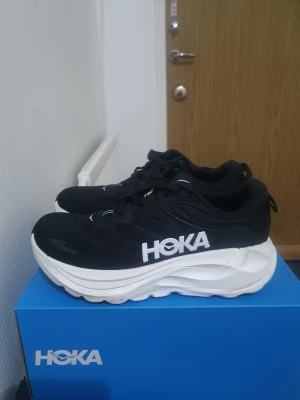 Hoka Gaviota 4 svarta sneakers - Svarta Hoka Gaviota 4 sneakers med vit, chunky sula och tydlig HOKA-logga på sidan. Skorna har en sportig design, snörning och är tillverkade i mesh och syntetmaterial för bra andningsförmåga och komfort. Perfekta för dig som gillar streetstyle och maximal dämpning.