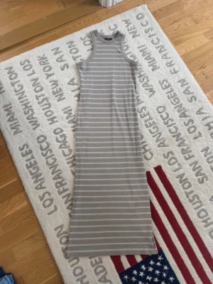 Gråvit randig långklänning - Snygg långklänning i grått med vita ränder. Ärmlös modell med rund halsringning och smal passform. Perfekt för en avslappnad och stilren look. Mjuk och bekväm, passar till många tillfällen.